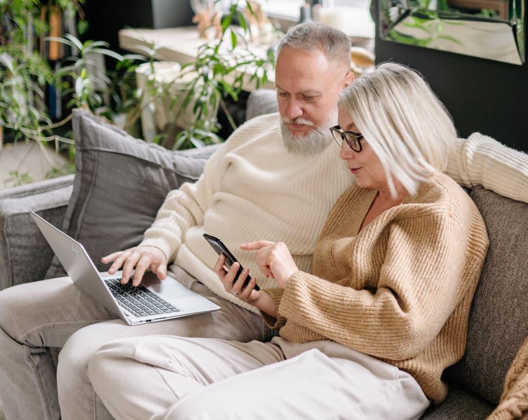 Mature couple looking at phone and computer discussing investment strategy